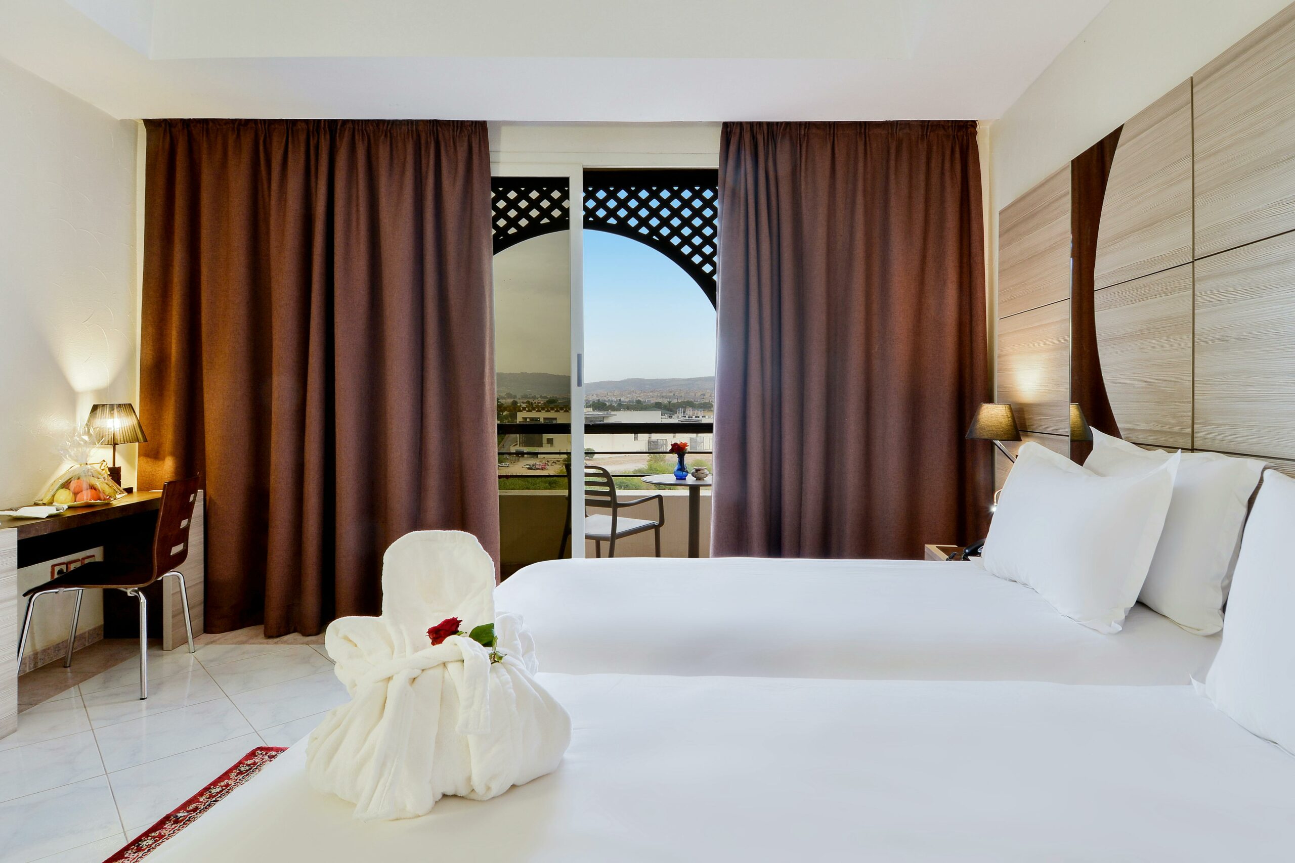 Elegant hotel room with two beds and balcony overlooking a scenic view. Ideal for travel and relaxation.