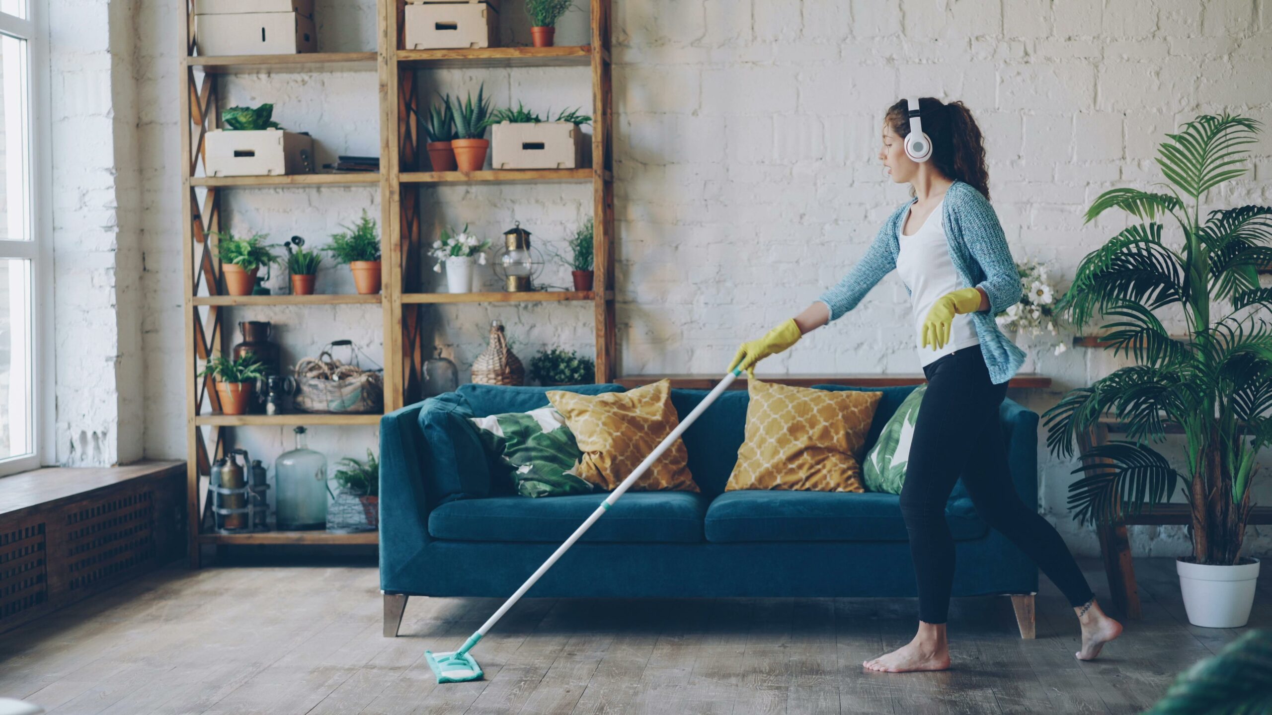 Woman wearing headphones and gloves while mopping a stylish indoor living room.